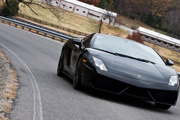 Ein schwarzer Lamborghini fährt auf der Straße mit Stoßstangen an den Rändern vor dem Hintergrund einer rustikalen Herbstlandschaft