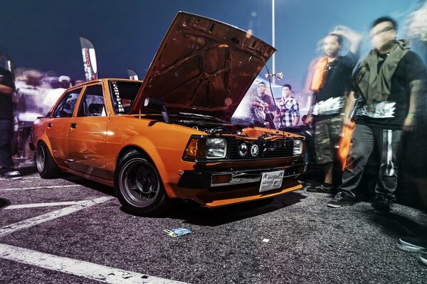 Ein orangefarbener Toyota Corolla. Menschen in Bewegung