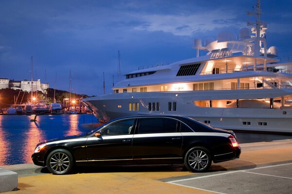 Luxuriöses schwarzes Auto auf dem Hintergrund einer großen weißen Yacht