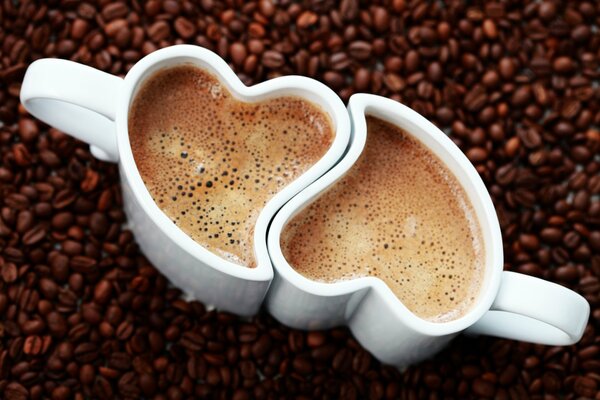 Zwei Tassen Kaffee mit Herzform auf Kaffeebohnen Hintergrund