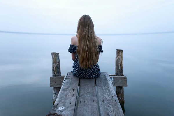 Langhaarige Mädchen sitzt am Wasser