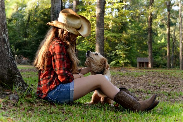 Mädchen mit Hut streichelt einen Hund unter einem Baum