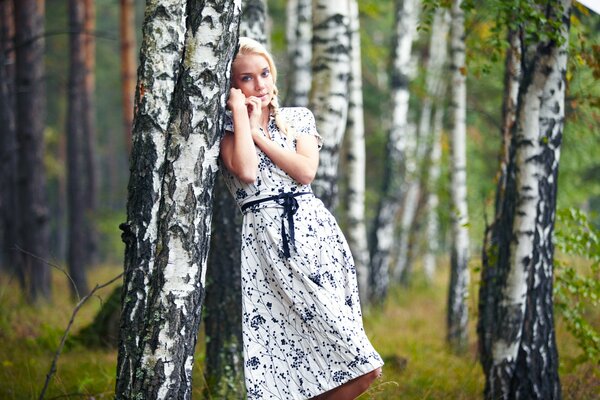 Schöne blonde Mädchen lehnte sich auf eine Birke