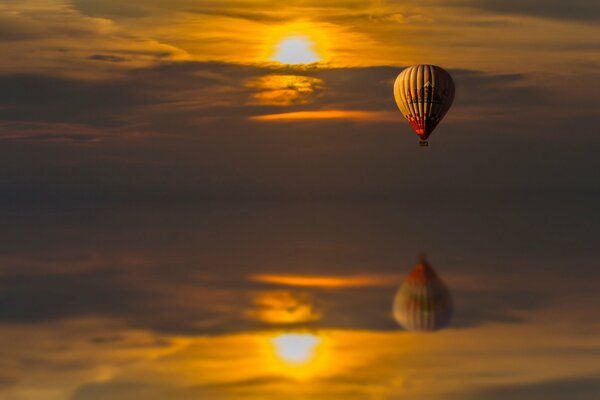 Reflexion im Wasser eines bei Sonnenuntergang fliegenden Ballons