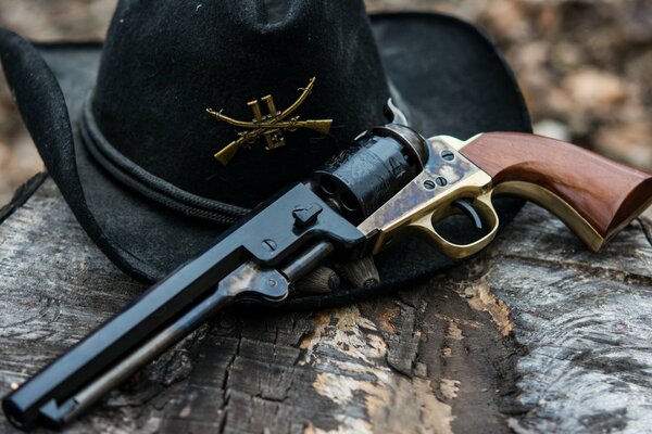 Ein schwarzer Hut und ein Revolver liegen auf der Baumrinde