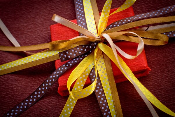 Die rote quadratische Geschenkbox ist mit gelben Bändern verbunden