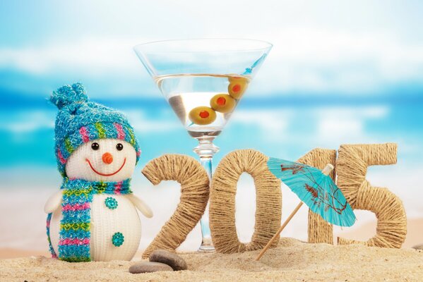 Zahlen 2015 am Strand, umgeben von einem Schneemann und einem Glas Martini mit einem Regenschirm